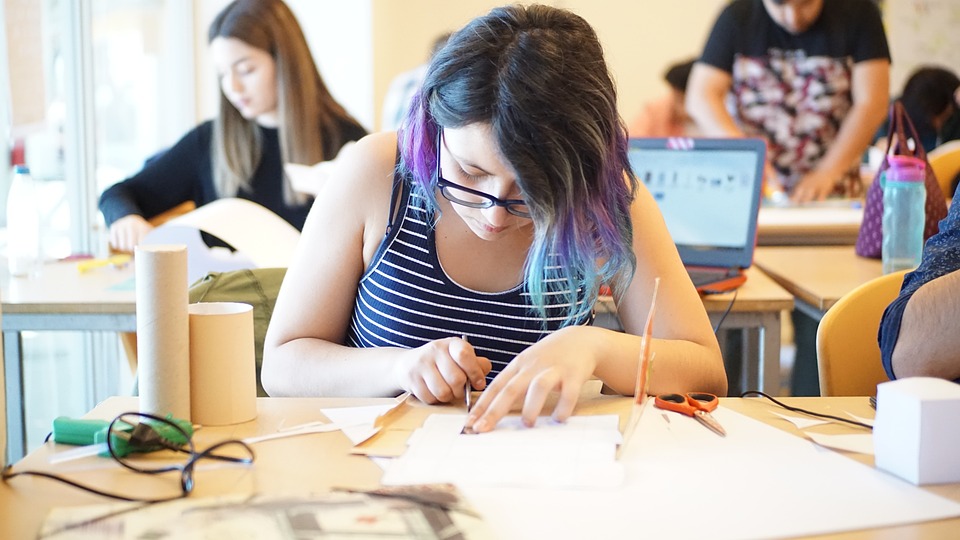 Classe di studentesse che studiano in classe. C'è una studentessa in primo piano che studia ed è china su un quaderno